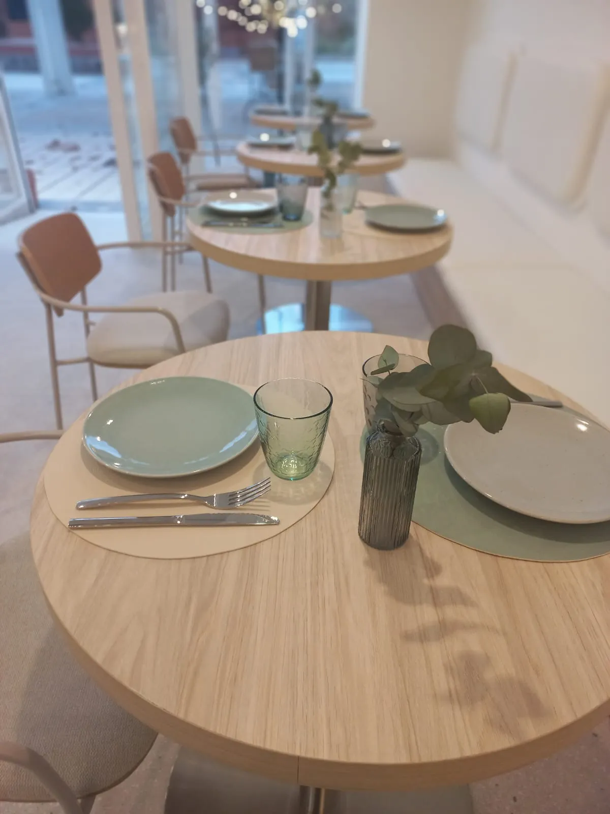 Mesa montada en la sala luminosa de La Alameda, con vajilla verde y eucalipto